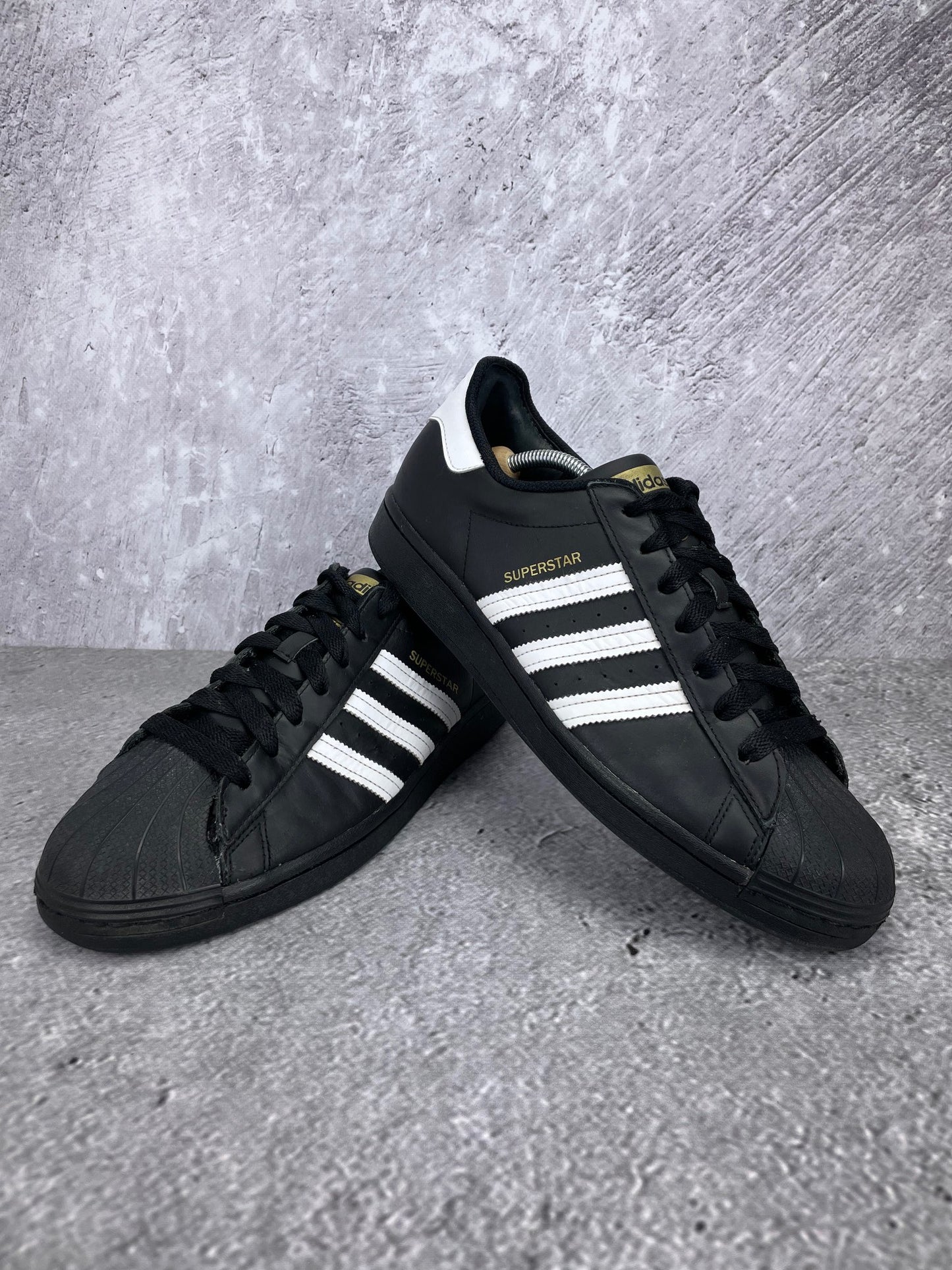 adidas Superstar “Core Black / Footwear White” Superstar Core Black - buty sportowe, para butów, widok z boku na tle studyjnym