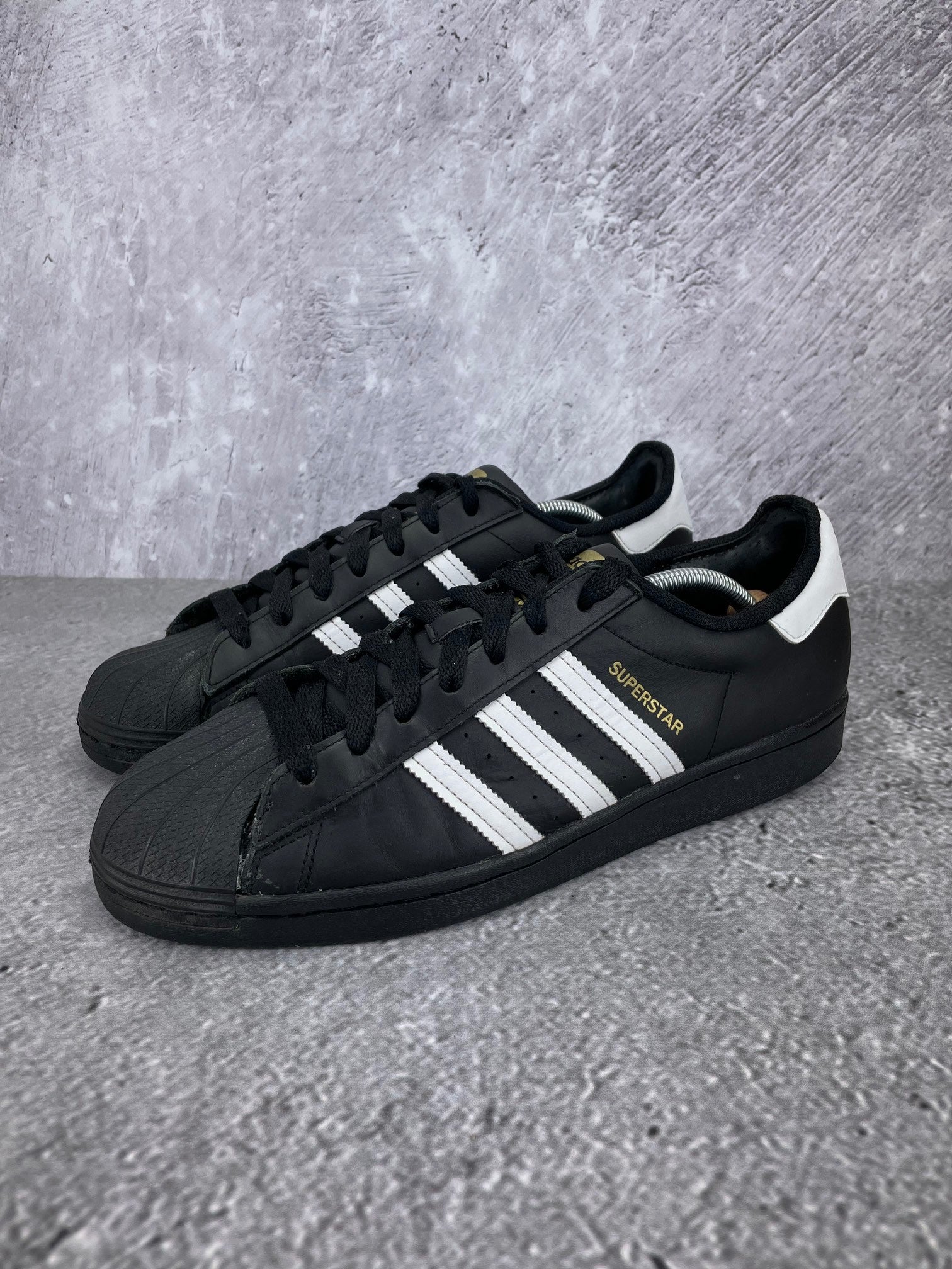 adidas Superstar “Core Black / Footwear White” Superstar Core Black - buty sportowe, widok z boku na tle studyjnym