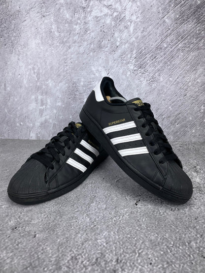 adidas Superstar “Core Black / Footwear White” Superstar Core Black - buty sportowe, para butów, widok z boku na tle studyjnym